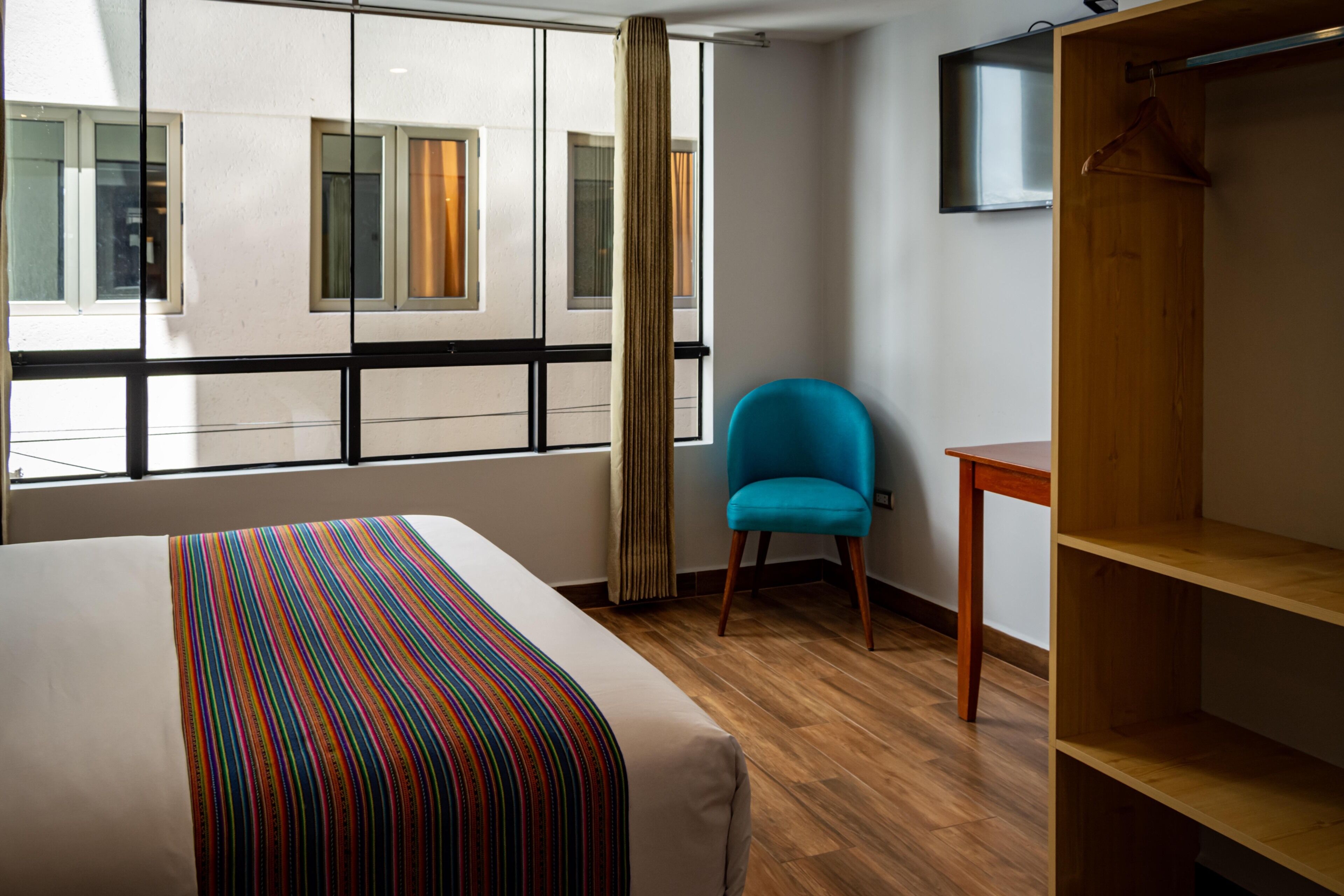 A hotel room with a bed, a blue chair, a wooden table, and a wardrobe.