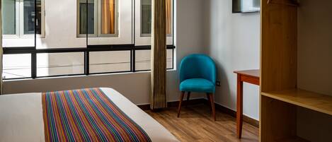 A hotel room with a bed, a blue chair, a wooden table, and a wardrobe.