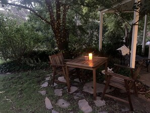 Une terrasse extérieure avec une table et des chaises en bois, entourée de chemins de pierre et d’une végétation luxuriante.