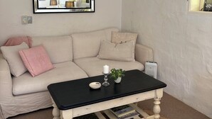 Un salon avec un canapé blanc, une table basse noire, un ventilateur de plafond, un miroir et une fenêtre agrémentée d’un lambrequin à rayures.