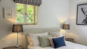 Une chambre à coucher bien rangée, avec un lit, deux tables de chevet, une fenêtre avec des rideaux et un tableau accroché au mur.