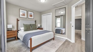 A bedroom with a bed, nightstands, a mirror, and a door leading to another room.