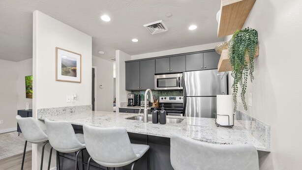 A modern kitchen with granite countertops, stainless steel appliances, and bar stools.