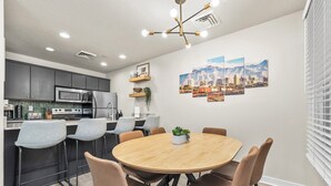 A modern kitchen with dark cabinets, a microwave, and a stove. There is a dining area with a round wooden table and brown chairs.