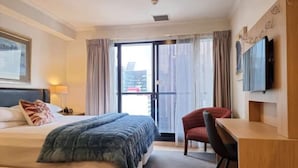 A hotel room with a bed, a desk, a chair, a television, and a large window with curtains. - Chic CBD Studio-Aircon-Wifi -Heated Pool (Auckland)
