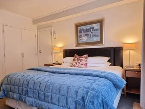 A hotel room with a large bed, a nightstand, a lamp, a wardrobe, and a framed picture on the wall. - Chic CBD Studio-Aircon-Wifi -Heated Pool (Auckland)