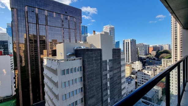 A cityscape with modern high-rise buildings, including a prominent glass building and a white building with a grid pattern. - Chic CBD Studio-Aircon-Wifi -Heated Pool (Auckland)