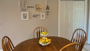 A dining area with a wooden table, chairs, and a bowl of fruit. There are wall decorations and a door labeled "Laundry".