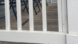 Een wit balkon met een leuning, een rode deur en een zwarte stoel.