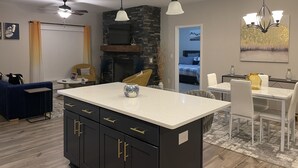 Een moderne keuken met een centraal kookeiland, zwarte kasten met gouden handgrepen en hanglampen.