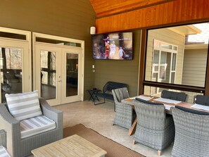 A covered outdoor seating area with wicker furniture, a television mounted on the wall, and sliding glass doors leading to the patio.