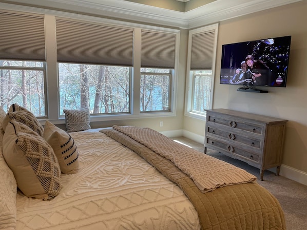 A bedroom with a large bed, multiple windows, a television, and a dresser.