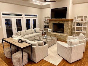A modern living room with a stone fireplace, a large flat-screen TV, and a cozy seating area with a sofa and armchairs.