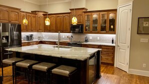 A modern kitchen with wooden cabinets, a large island with bar stools, stainless steel appliances, and pendant lighting. - Luxury Lake Lanier Estate + Double Dock (Gainesville)