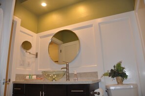 A bathroom with a round mirror, a glass bowl sink, a toilet, and a potted plant.