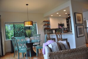 A modern kitchen with white cabinets, a stone backsplash, and a dining area with teal chairs and a glass table.