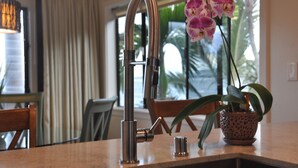 Una cocina con un grifo moderno, una orquídea en maceta y vistas a palmeras a través del ventanal.
