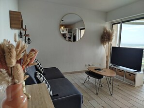 A modern living room with a sofa, a round mirror, a television, and a view of the ocean. - Fall in love with this cosy one-bedroom flat with stunning sea views - 4GSUD101 (CANET PLAGE)