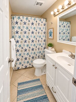 A bathroom with a starfish shower curtain, a white toilet, a sink with a mirror, and a striped rug.