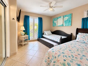 A bedroom with a bed, a nightstand, a ceiling fan, a window with curtains, and a wall-mounted artwork.