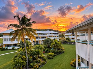 A hotel with multiple-story buildings, a well-maintained lawn, and a sunset view.