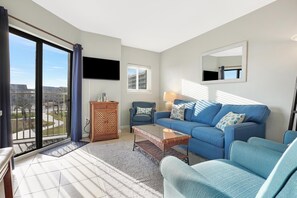 Relax in this stylish living room with a comfortable sofa, flat-screen TV, and sliding glass door leading to an outdoor area with a view.