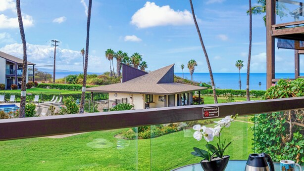 Une vue depuis un balcon donnant sur une piscine, des palmiers et un bâtiment doté d’un toit en pente.