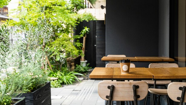 An outdoor cafe with wooden tables and chairs, a coffee cup on one table, and lush greenery in the background. - HOTEL RINGS KYOTO (Kyoto)