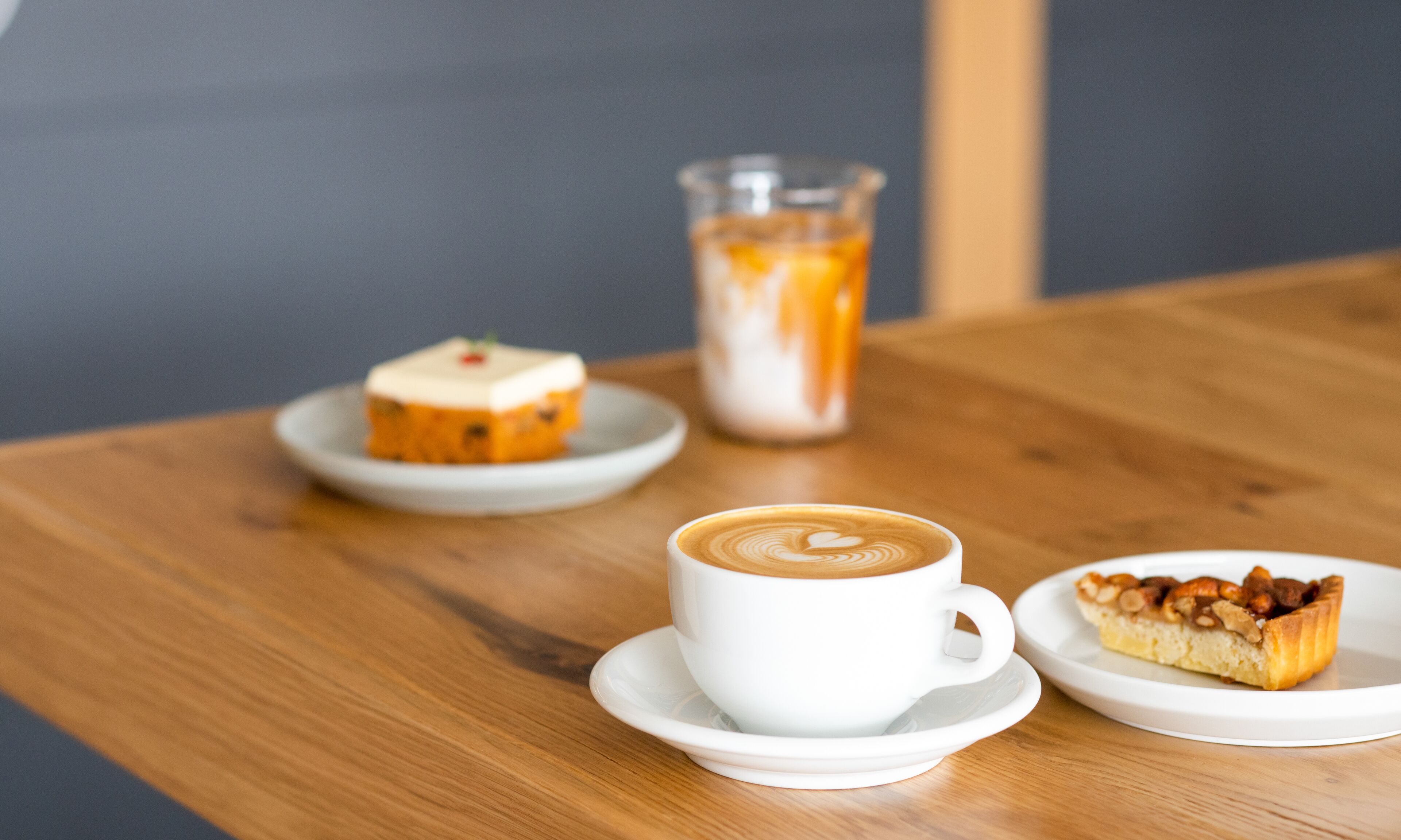Una mesa con una taza de café, un vaso de café helado y dos platos pequeños de comida.