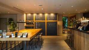 A modern restaurant with a wooden bar and stools, a menu board, and a view of the outdoors. - HOTEL RINGS KYOTO (Kyoto)