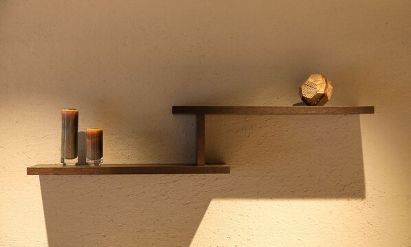 Una repisa de madera con dos objetos cilíndricos y un objeto hexagonal frente a una pared texturizada.