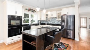 Une cuisine moderne avec des meubles blancs, un îlot central noir, des appareils en acier inoxydable et des luminaires suspendus.
