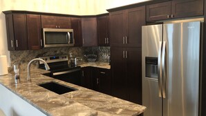 A modern kitchen with dark wooden cabinets, stainless steel appliances including a microwave and refrigerator, a granite countertop, and a built-in oven. - Newly constructed modern home with luxurious rooftop patio (Tallahassee)