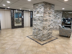 A lobby with a tiled floor, a stone pillar, a mirrored wall, and a patterned armchair.