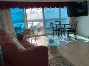 A living room with a red sofa, a glass coffee table, and a balcony with a view of the sea. - Panoramic Ocean and River View
 26SW (DAYTONA BEACH SHORES)
