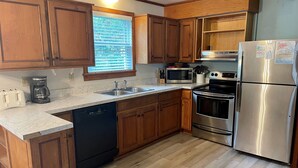 A modern kitchen with wooden cabinets, stainless steel appliances, a dishwasher, and a window with blinds. - Island Cat: This spacious and comfortable island home (Ocracoke)