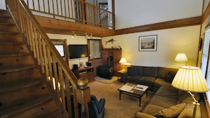 A spacious living area with a wooden staircase, a large sofa, a coffee table, and a fireplace. - Island Cat: This spacious and comfortable island home (Ocracoke)
