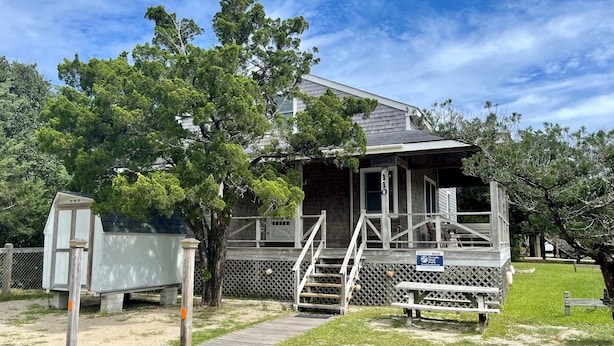 A small, single-story building with a porch and a wooden deck. - Island Cat: This spacious and comfortable island home (Ocracoke)