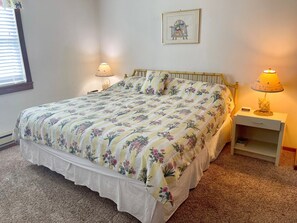 A bedroom with a floral bedspread, two bedside lamps, a framed picture on the wall, and a bedside table with a lamp and a decorative item.