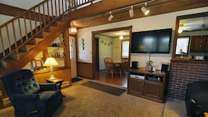 A living room with a wooden staircase, a television, a dining area, and a fireplace. - Island Cat: This spacious and comfortable island home (Ocracoke)