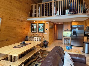 A wooden interior with a dining area, kitchen, and a loft space.