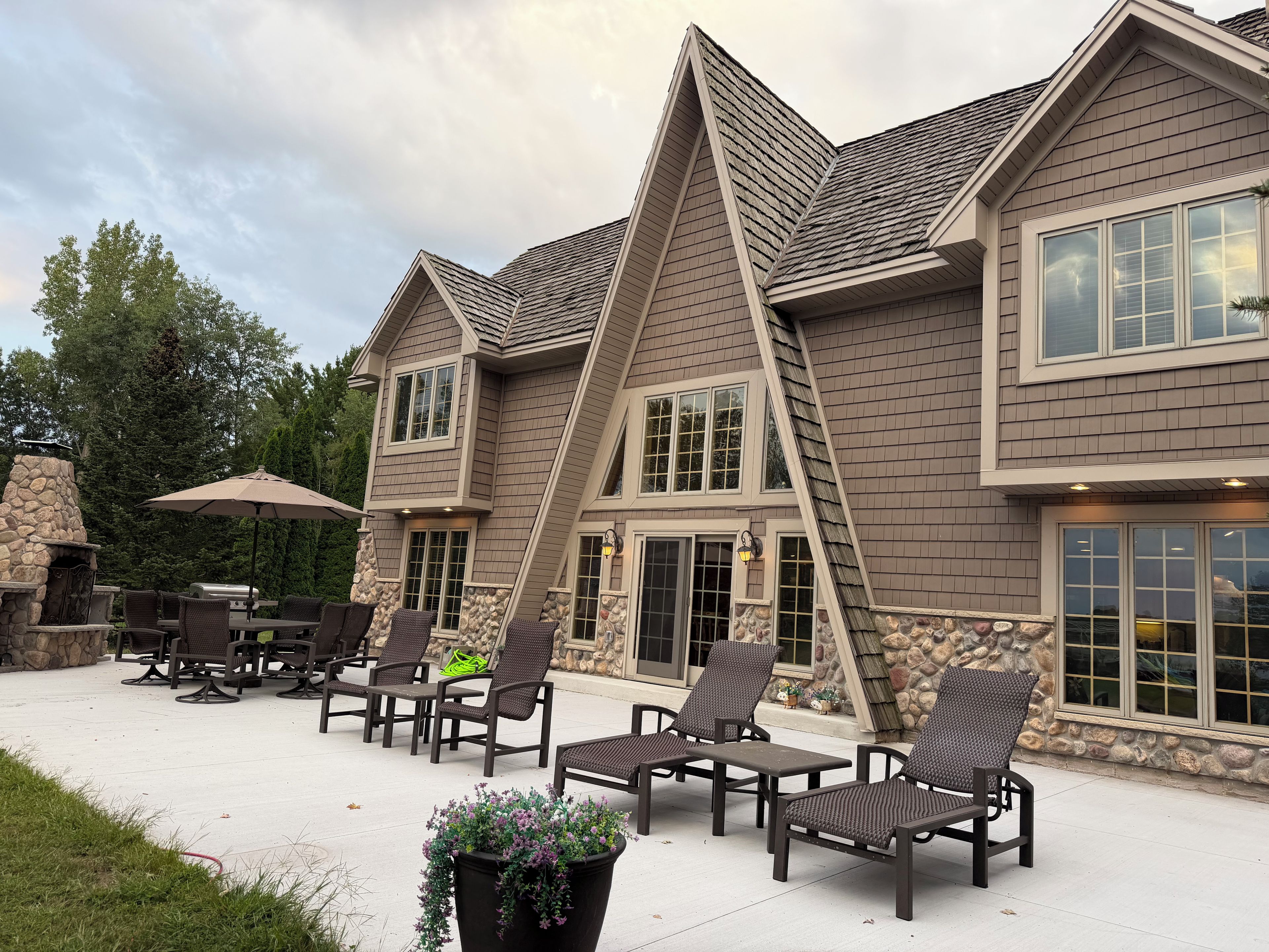 A two-story house with a stone fireplace, outdoor seating, and large windows.
