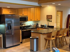 A modern kitchen with stainless steel appliances, wooden cabinets, and a bar area with bar stools.