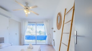 A hotel room with a bed, a ceiling fan, a window with curtains, a view of the outside, and a wooden ladder. - 2Br. Apartment, 100m from Beaches, Terrace & Parking (Cannes)