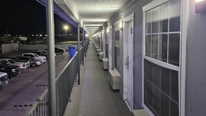 A corridor with a row of rooms on one side, a parking area on the other, and a covered walkway. - Motel 9 (Laredo)