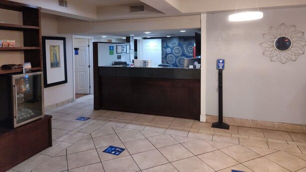 A hotel reception area with a reception desk, framed artwork on the walls, and a decorative wall piece. - Motel 9 (Laredo)