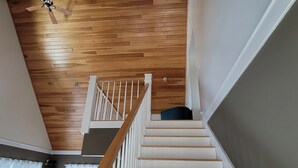 A staircase with wooden steps and white railings, leading to a landing with a ceiling fan.