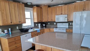 A kitchen with wooden cabinets, a granite countertop, a microwave, a stove, a dishwasher, and two stools.
