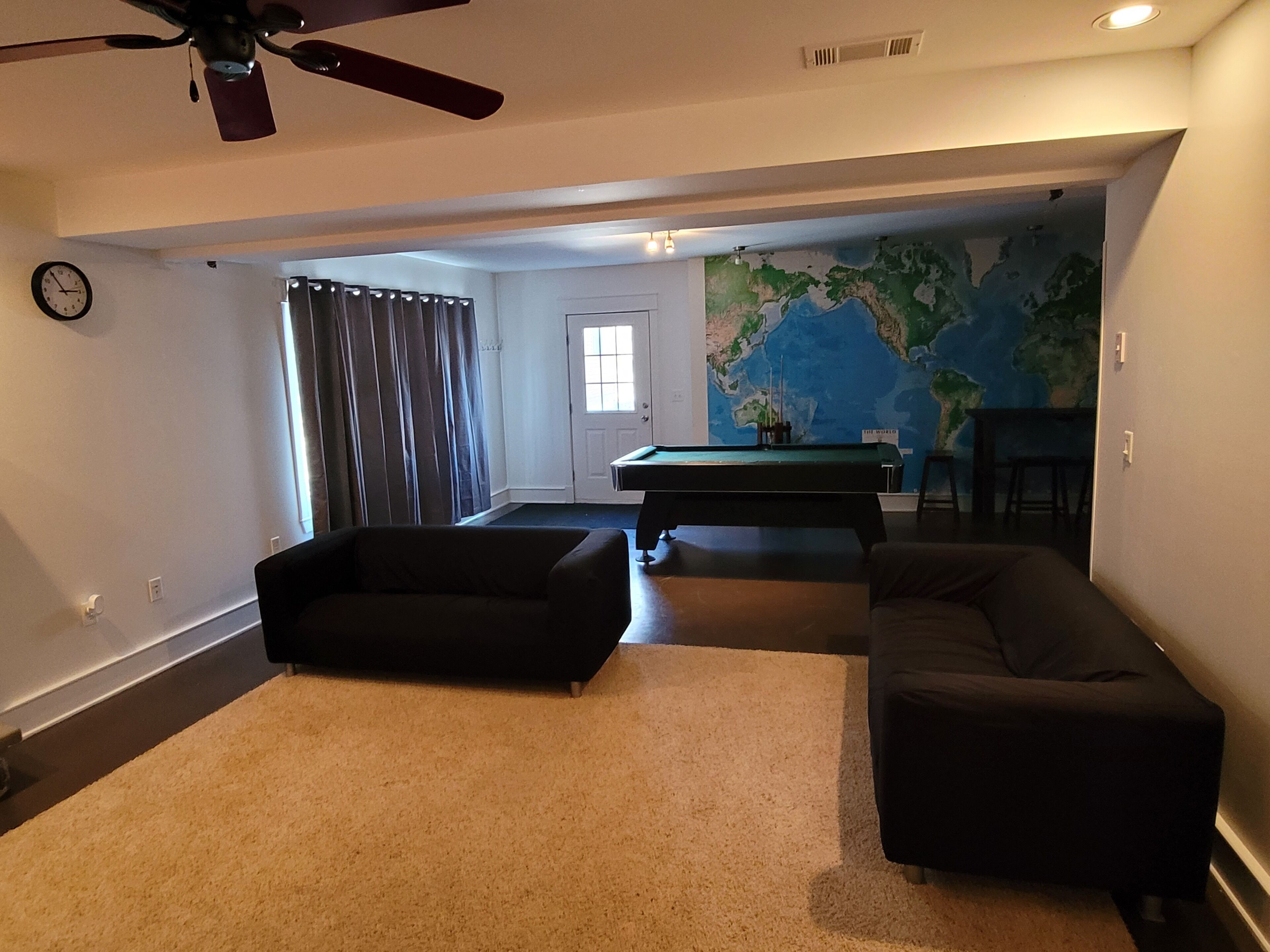 Una sala de estar con mesa de billar, dos sofás, ventilador de techo y un mapa del mundo en la pared.