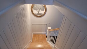 A wooden staircase with white paneling on the walls, leading to a landing with a white railing.